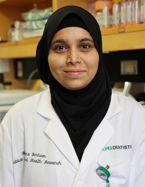 Woman with black head wrap and nose piercing wearing a white coat in a lab setting